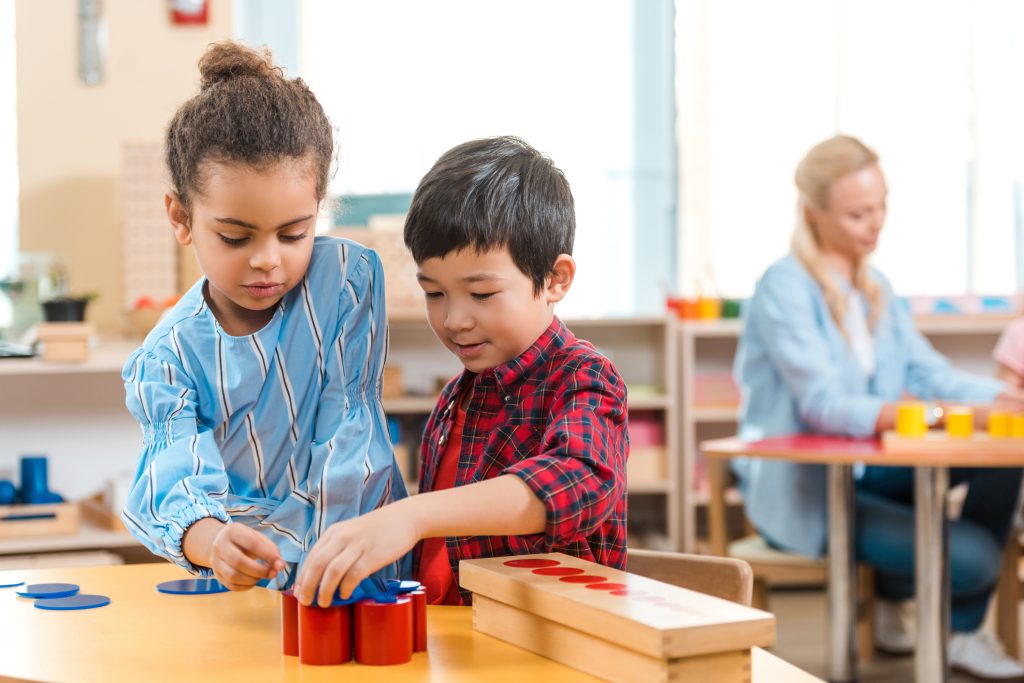 Selective focus of kids folding educational game with teacher at background in montessori class